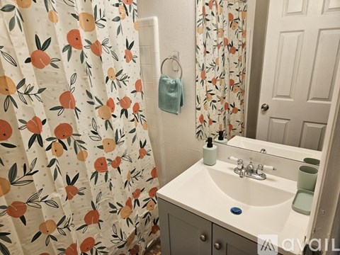 A bathroom with a sink, mirror, and shower curtain with fruit pattern.