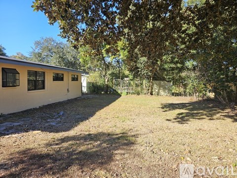 A house with a brown roof and white walls is surrounded by trees and grass.