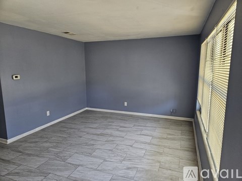A room with grey tiled flooring and a window with blinds.