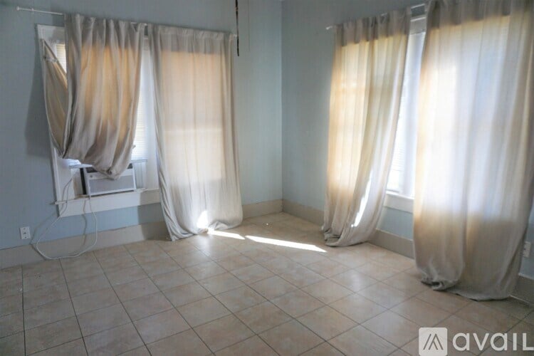 A room with two windows covered by sheer curtains.