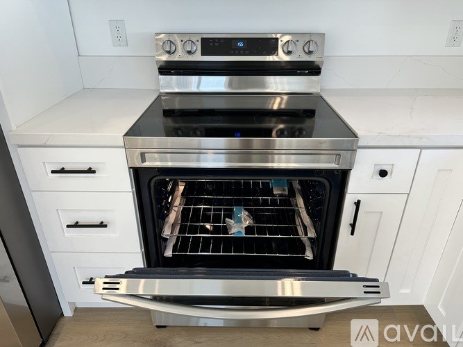 A modern stainless steel oven with a digital display is built into a white kitchen cabinet.