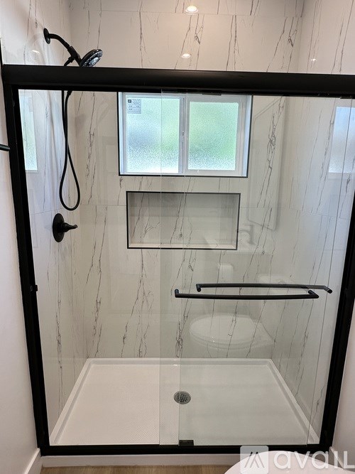 A bathroom with a glass shower door and a marble wall.