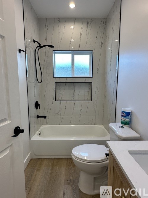 A white toilet sits in a bathroom with a marble wall and a window.