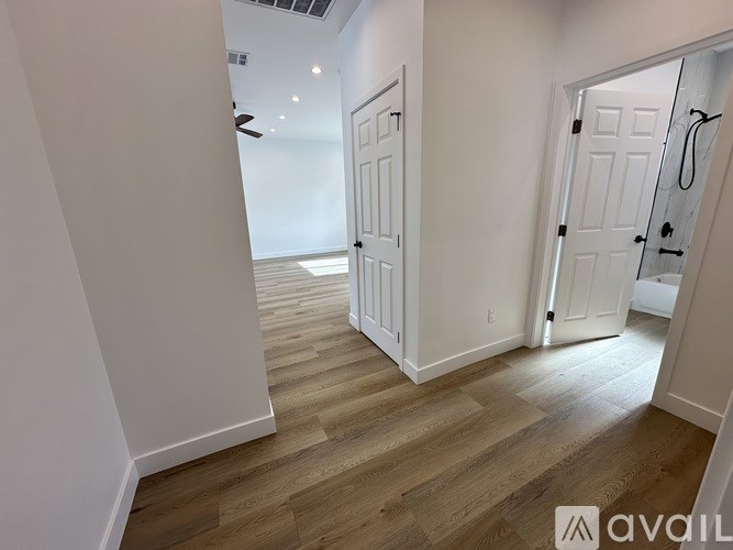 A room with white walls and wooden flooring, with a door on the right and a ceiling fan above.