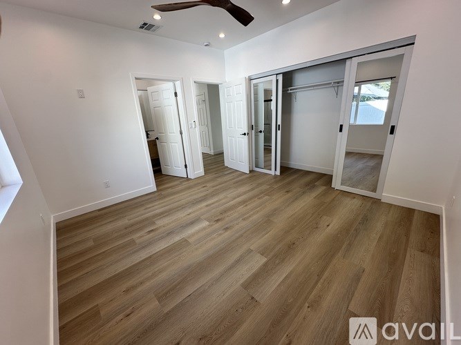 A room with wooden flooring and white walls, with a ceiling fan and three doors.
