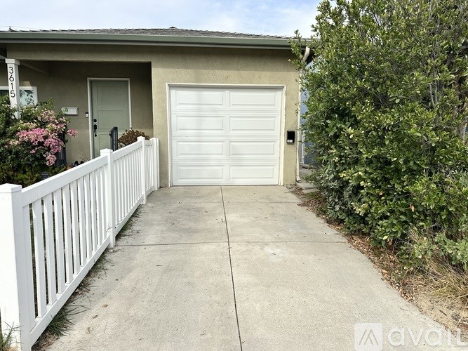 A white fence leads to a garage door of a house.
