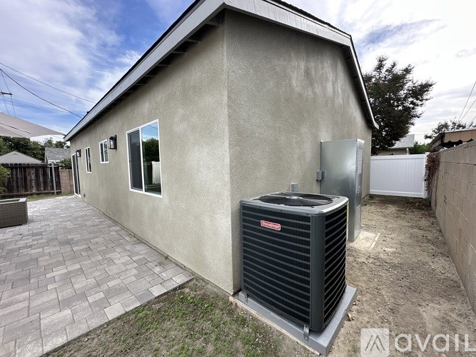 A house with a grey wall and a black air conditioner unit in front of it.