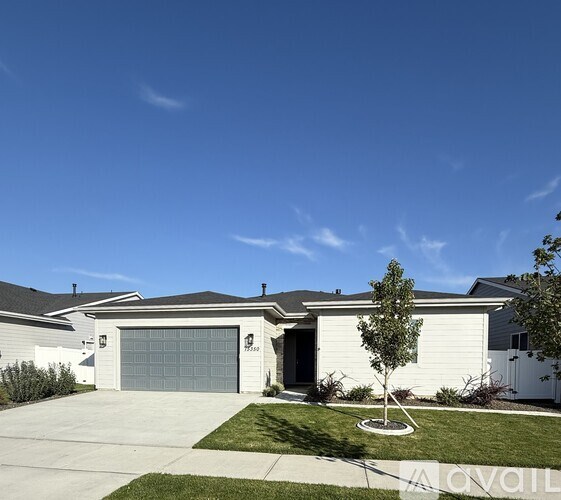 A white house with a grey garage door and a tree in front.