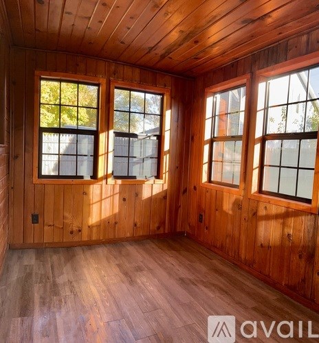 A room with wooden walls and floors and two windows.