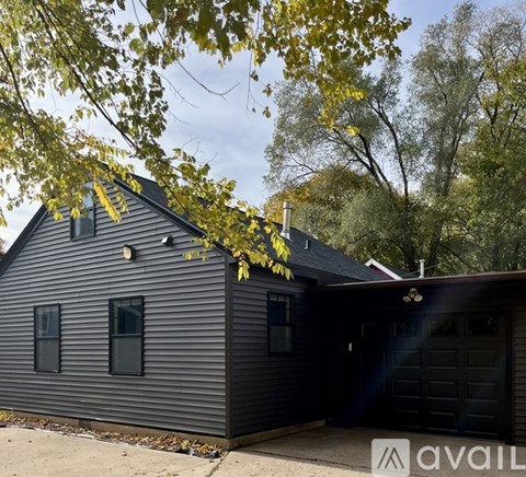 A black house with a garage is surrounded by trees.