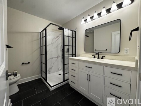A bathroom with a marble shower and white cabinets.