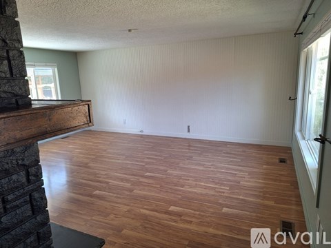 A room with wooden flooring and a fireplace on the left side.