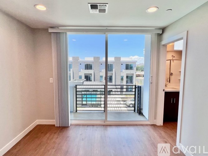 A room with a sliding glass door leading to a balcony with a view of buildings outside.