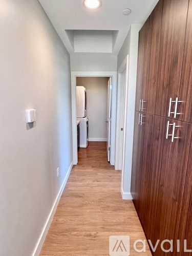 A hallway with wood flooring and a white wall with a switch.