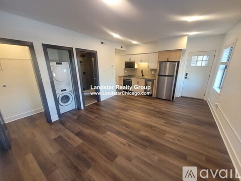 A spacious room with wooden flooring and a kitchen area in the background.