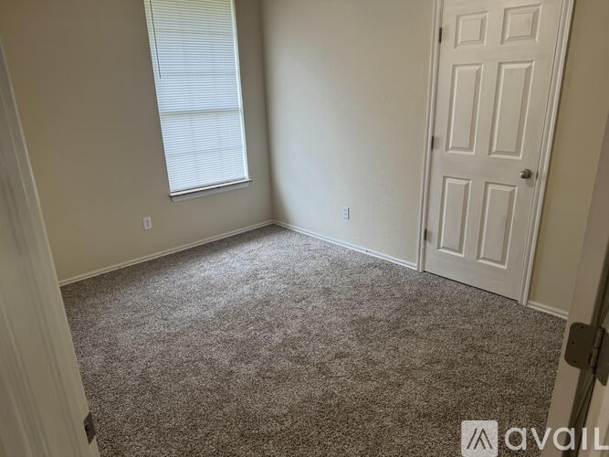 A room with a carpeted floor, a door, and a window with blinds.