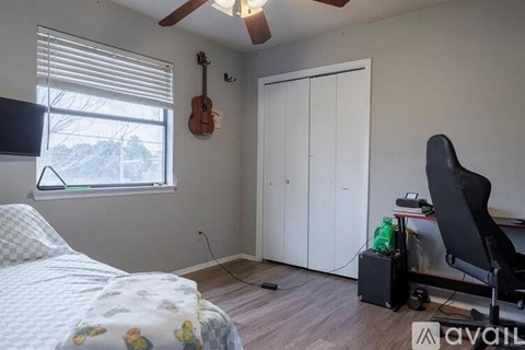 A room with a bed, a chair, and a guitar hanging on the wall.
