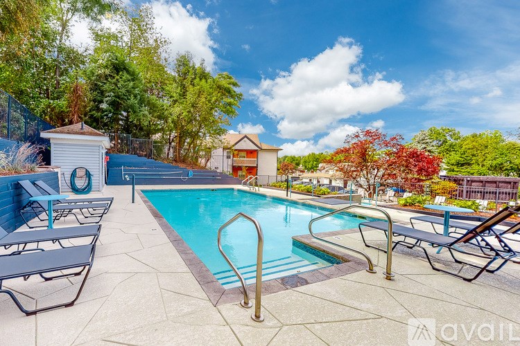A pool surrounded by trees and chairs with a fence and a small building in the background.