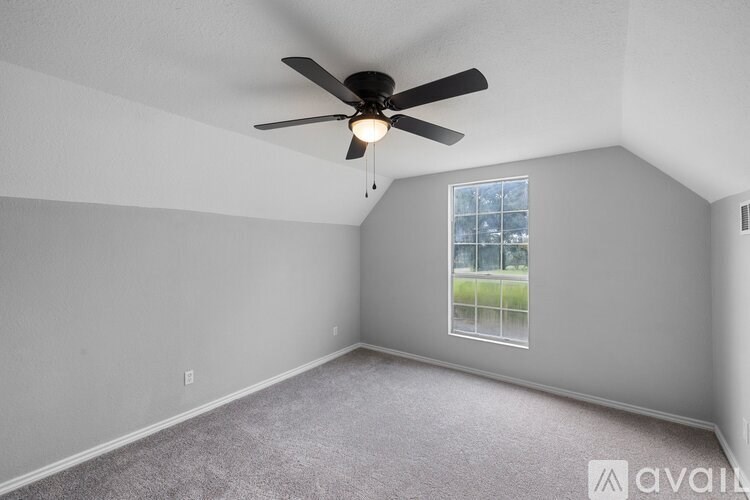 A room with a ceiling fan and a window showing a green outdoor area.