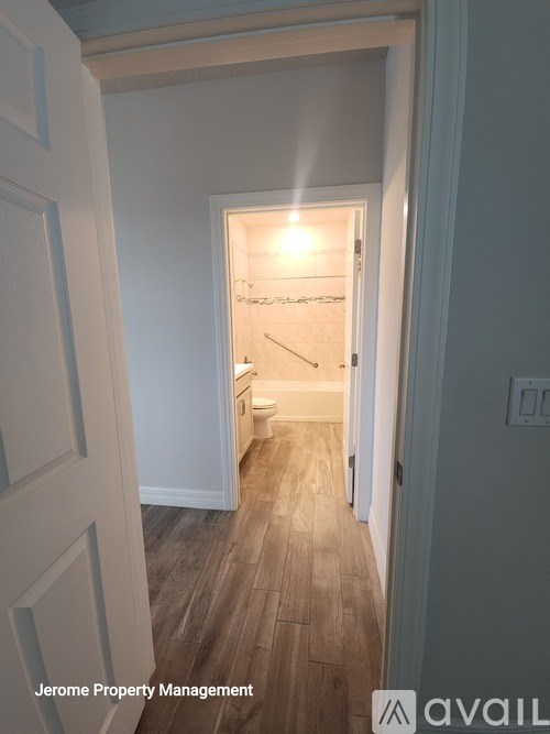 A hallway with wood flooring and white walls leading to a bathroom.