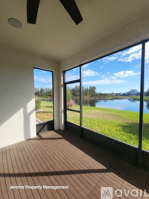 A room with a wooden floor and a ceiling fan, overlooking a lake.