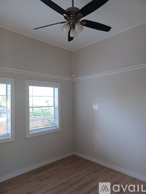 A room with a ceiling fan and two windows.