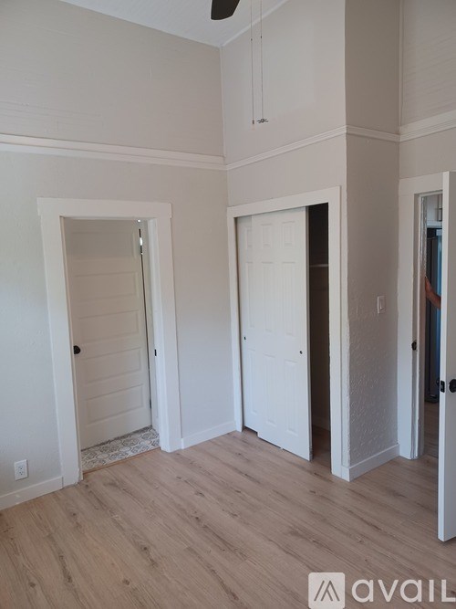A room with white walls and wooden flooring, with a door on the left and a partially open door on the right.