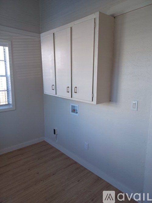 A room with wooden floors and white walls with a window and a set of white cabinets.