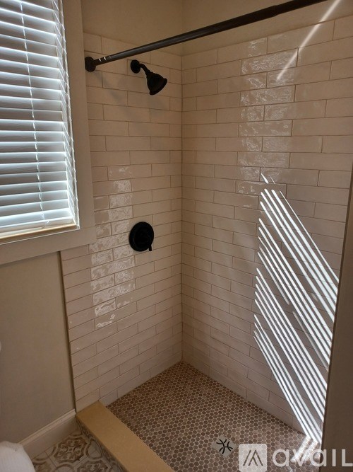 A bathroom with a shower and a window with blinds.