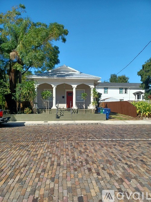 A white house with a red door and a brick driveway.
