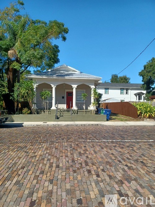A white house with a red door and a brick driveway.