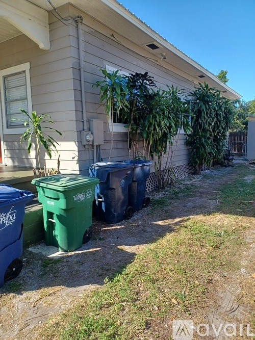 A house with a green recycling bin in front of it.