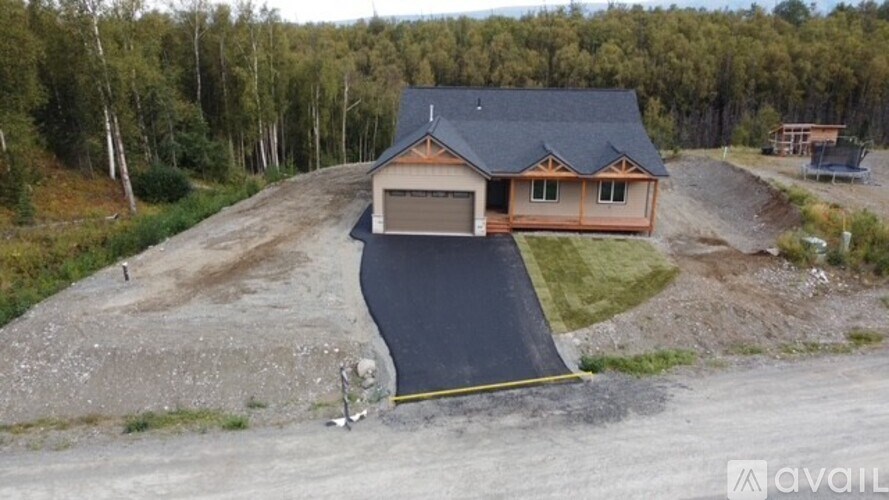 A house with a black roof and a brown garage door is surrounded by a gravel driveway.