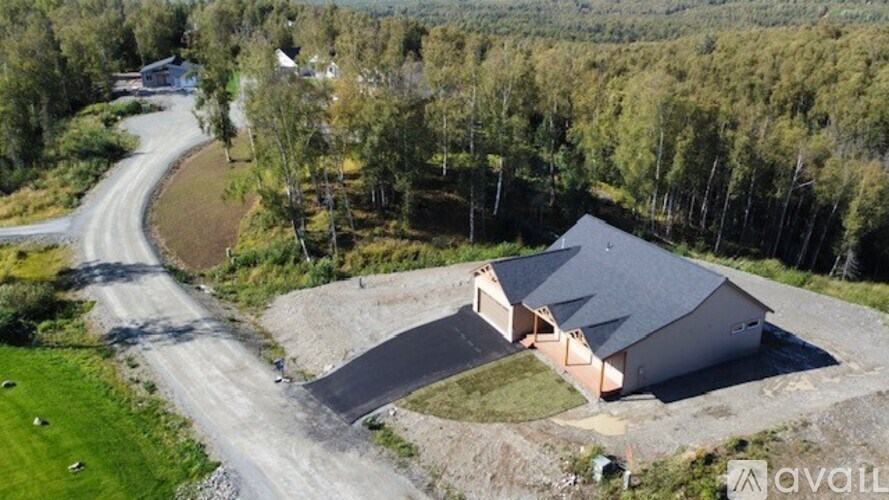 A house with a grey roof is surrounded by trees and a road.