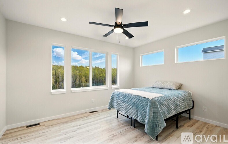 A bedroom with a bed, a ceiling fan, and a view of trees through the windows.