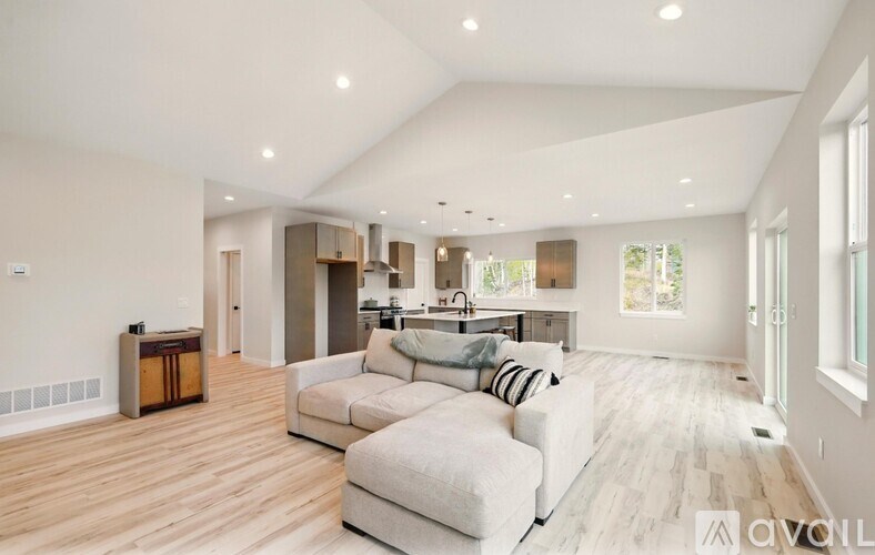 A spacious living room with a white couch and a kitchen in the background.