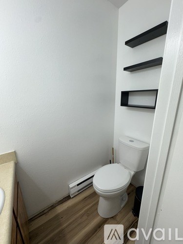 A white toilet in a small bathroom with a wooden floor and a white wall.