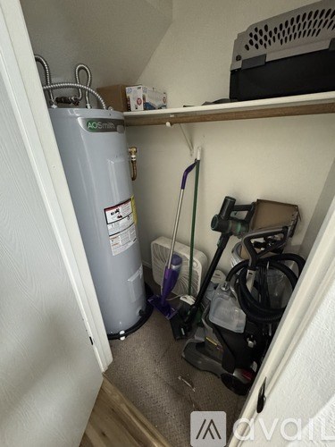 A room with a grey AO Smith tank and a vacuum cleaner.
