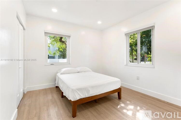 A bedroom with a bed, wooden flooring, and two windows.