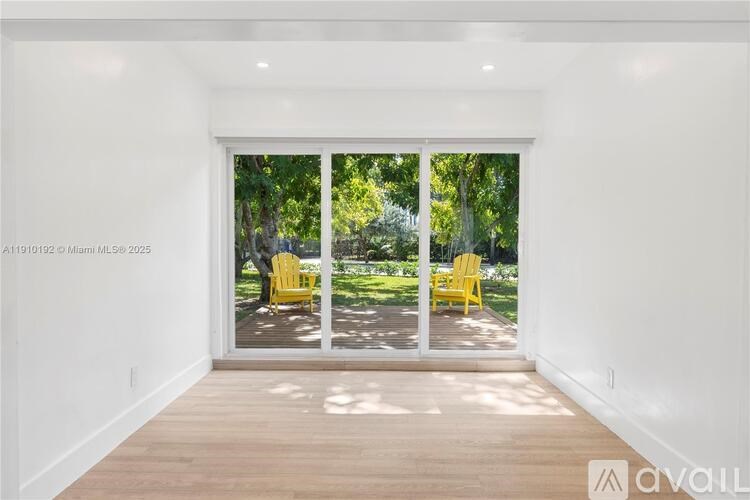 A room with a sliding glass door leading to a backyard with two yellow chairs.