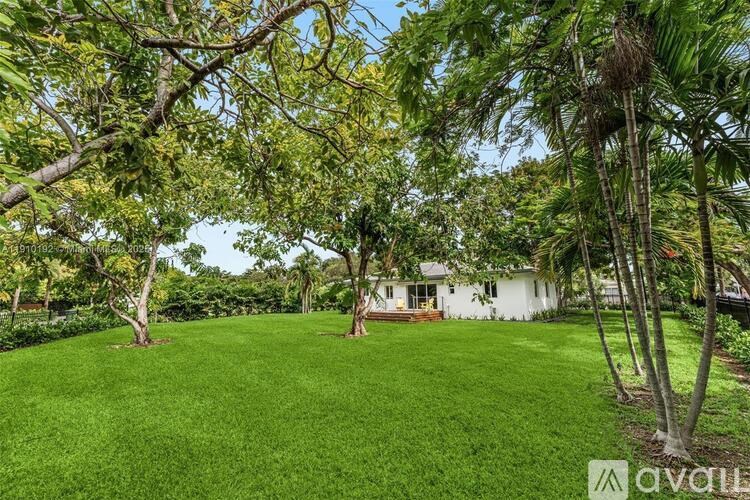 A lush green lawn with a white house and trees in the background.