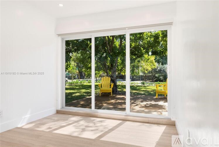 A room with a sliding glass door leading to a garden with a yellow chair.