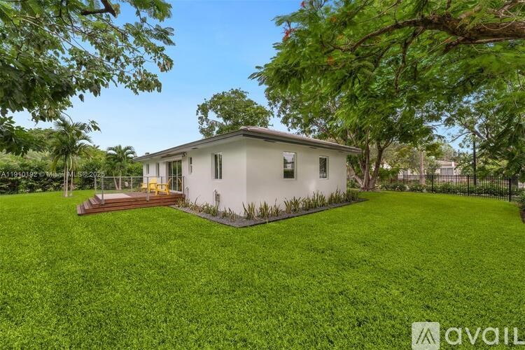 A house with a white exterior and a green lawn is surrounded by trees.