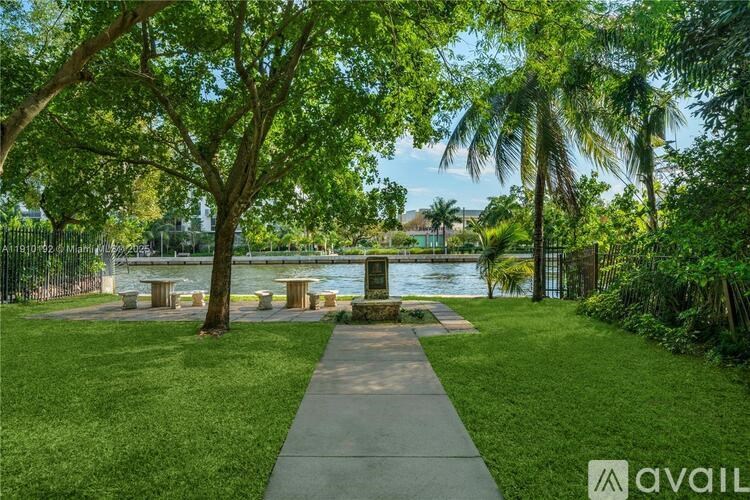 A park with a walkway, trees, and a body of water.