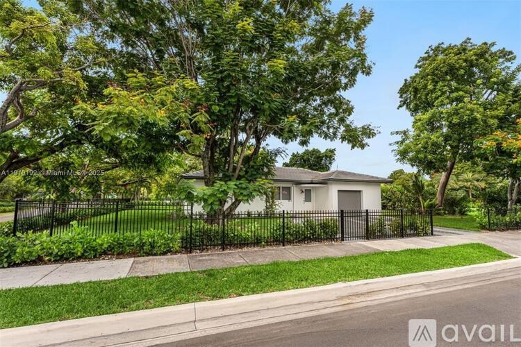 A house with a black fence and green trees in front.