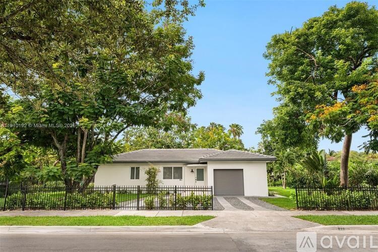 A white house with a black fence and trees in the background.