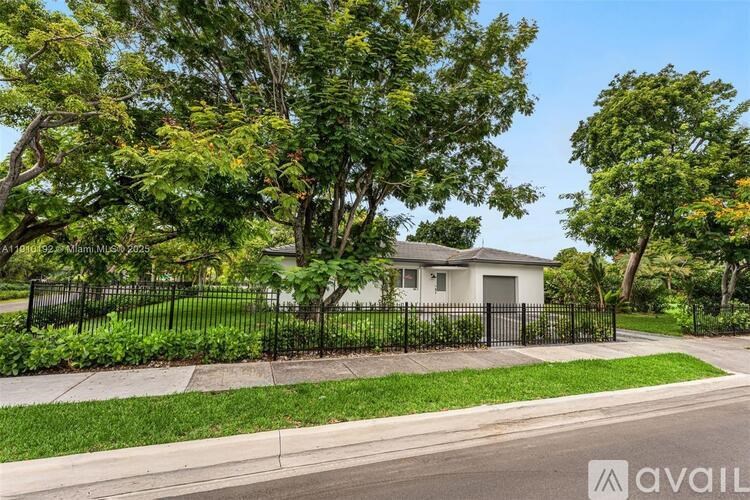 A house with a black fence and green trees in front.