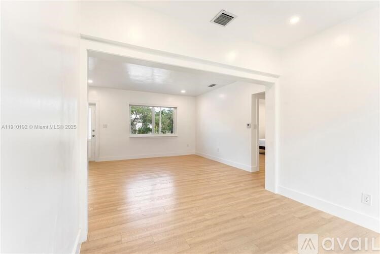 A spacious room with wooden flooring and white walls, with a window showing greenery outside.