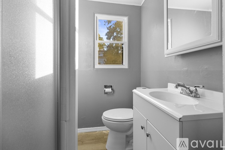 A bathroom with a toilet, sink, and a window with a view of trees.