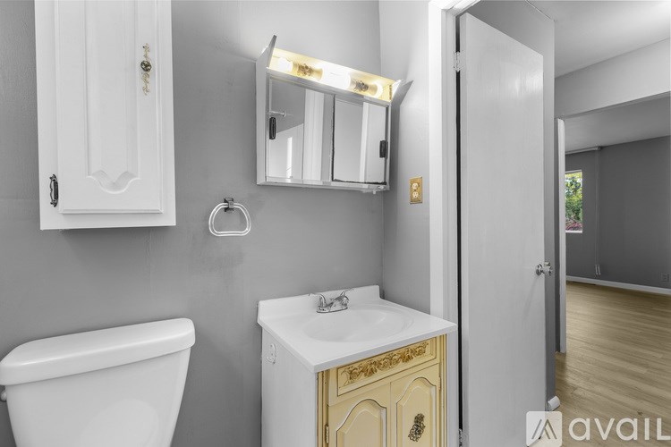 A bathroom with a white toilet and a white sink with a gold cabinet.